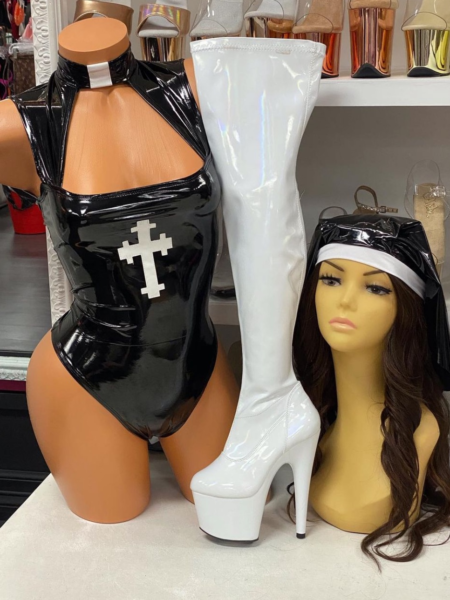 Misbeheaven Nun Costume Bodysuit in glossy black patent-look material with a white cross, high collar, chest cutout, and fitted high-cut bottom.