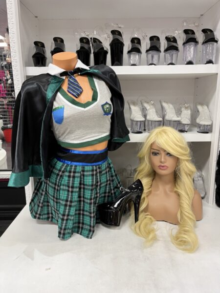 Sinister Spellcaster Costume Set with cropped school uniform top, green plaid pleated skirt, striped tie, crest detail, and dark cape.
