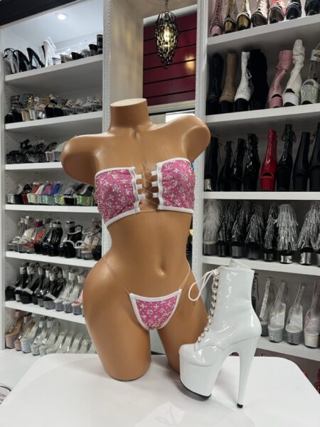 Pink monogram cutout two-piece outfit with bandeau top and micro bottom, displayed on mannequin with white platform lace-up boot