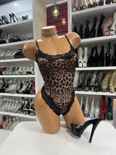 Leopard lace bodysuit with sheer mesh fabric and black lace trim displayed on a mannequin with black platform heels in a boutique setting