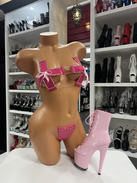 A pink rhinestone two-piece set featuring a cross-style bra and matching micro thong. Satin bows and sparkle details create a bold, flirty look.
