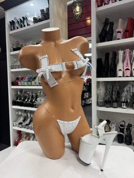 White rhinestone strappy micro bikini set with cross straps and bow accents displayed on mannequin in boutique showroom