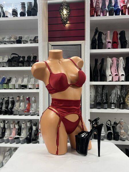 Red satin lingerie set with structured bra, high-waist garter belt, adjustable straps, and matching thong displayed on mannequin in boutique showroom
