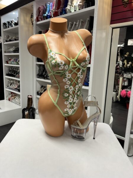 The Green Daisy Lace Bodysuit features sheer mesh, embroidered floral details, and a lace-up front for a flattering fit. This piece blends playful style with bold design.