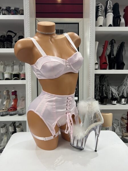 Light pink satin garter set featuring an underwire balconette bra, lace-up high-waisted garter panty, adjustable garter straps, and a coordinated three-piece lingerie design.