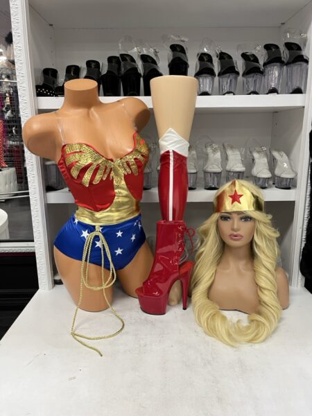 What A Woman Costume by Forplay featuring a red and gold superhero crop top, blue star-print high-waisted bottoms, gold wrist cuffs, red and white leg accessories, gold headpiece, and matching lasso.
