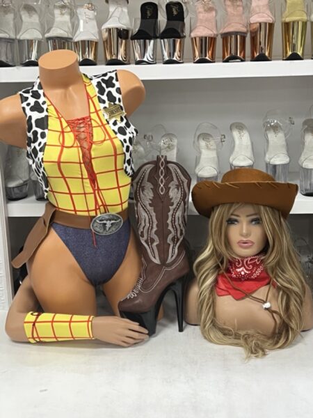 Western Doll Cowgirl Costume featuring yellow plaid romper, cow-print vest with badge, wrist cuffs, red bandana, brown hat, and belt.