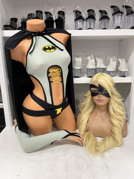 Batgirl inspired superhero costume featuring a gray asymmetrical bodysuit with black trim, yellow lace-up front, black cape, superhero eye mask, and matching arm accessory.