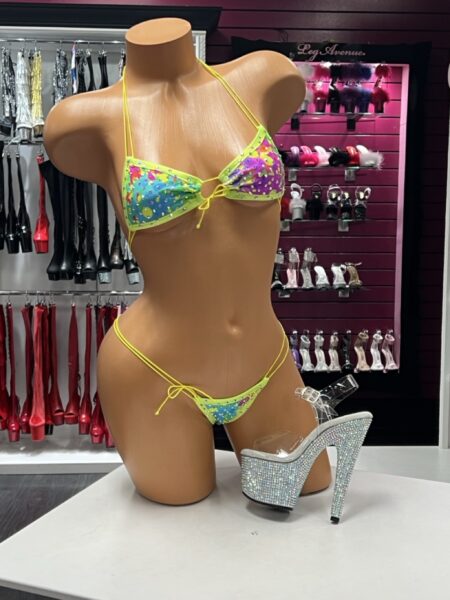 Neon Splash Crystal Bikini featuring a colorful blue, purple, pink, and yellow splash print, sparkling crystal accents, neon yellow halter straps, and matching side-tie thong bottom.